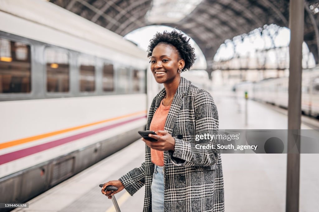 Young black women with suitcase on the train station using mobile phone