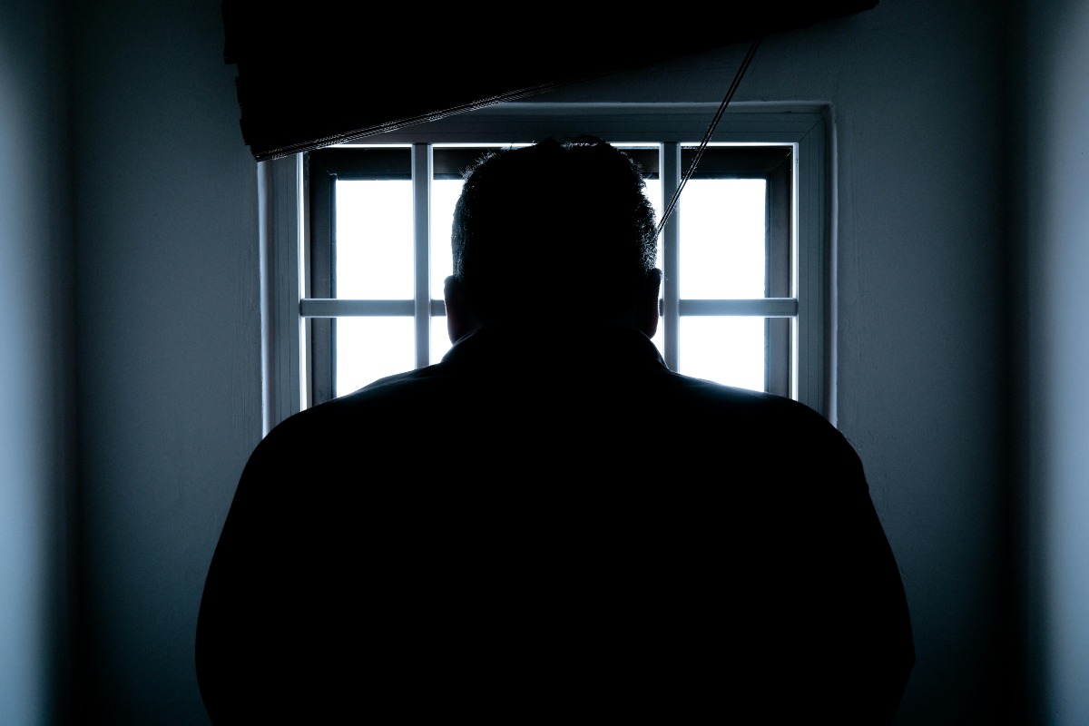 Rear view of a man's silhouette in jail looking out a window.