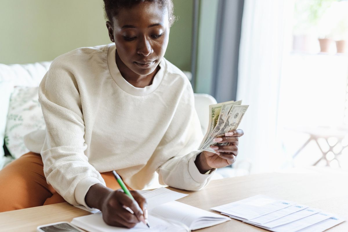 woman counting money while writing on a notepad