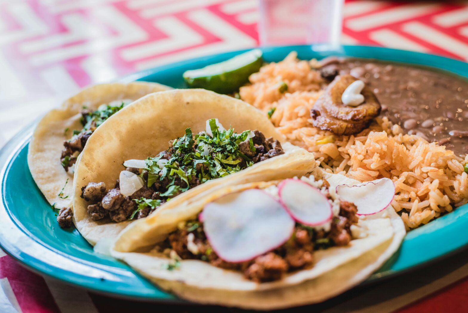 A blue plate holding Mexican tacos, rice, and beans.