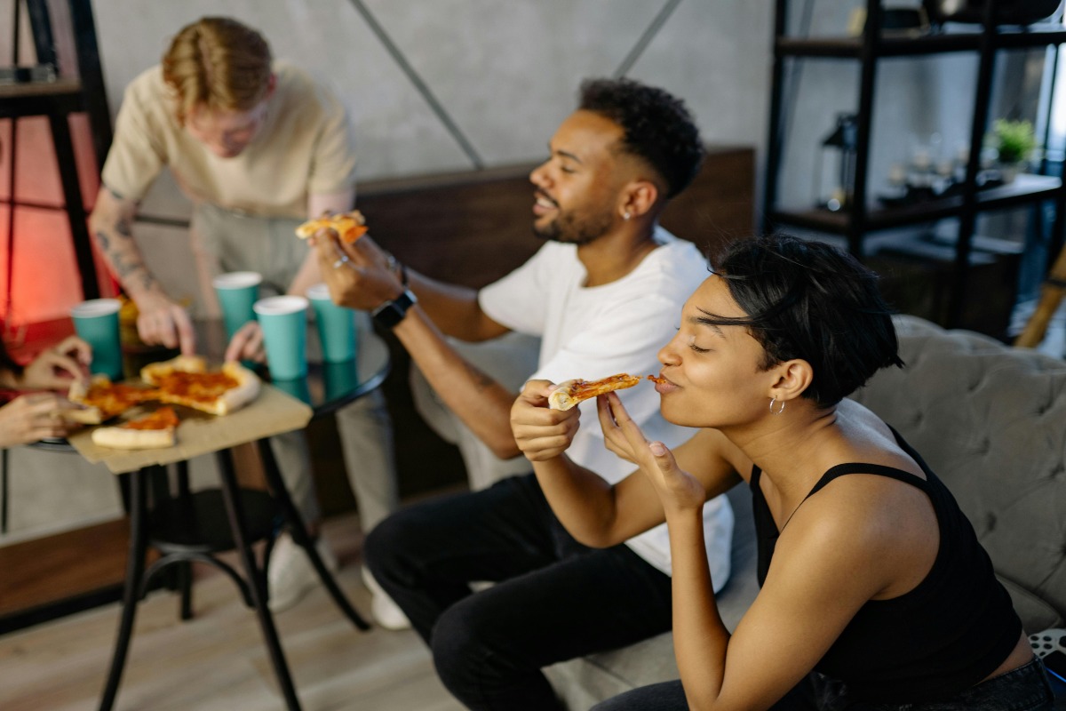 Friends sitting on a couch eating pizza.