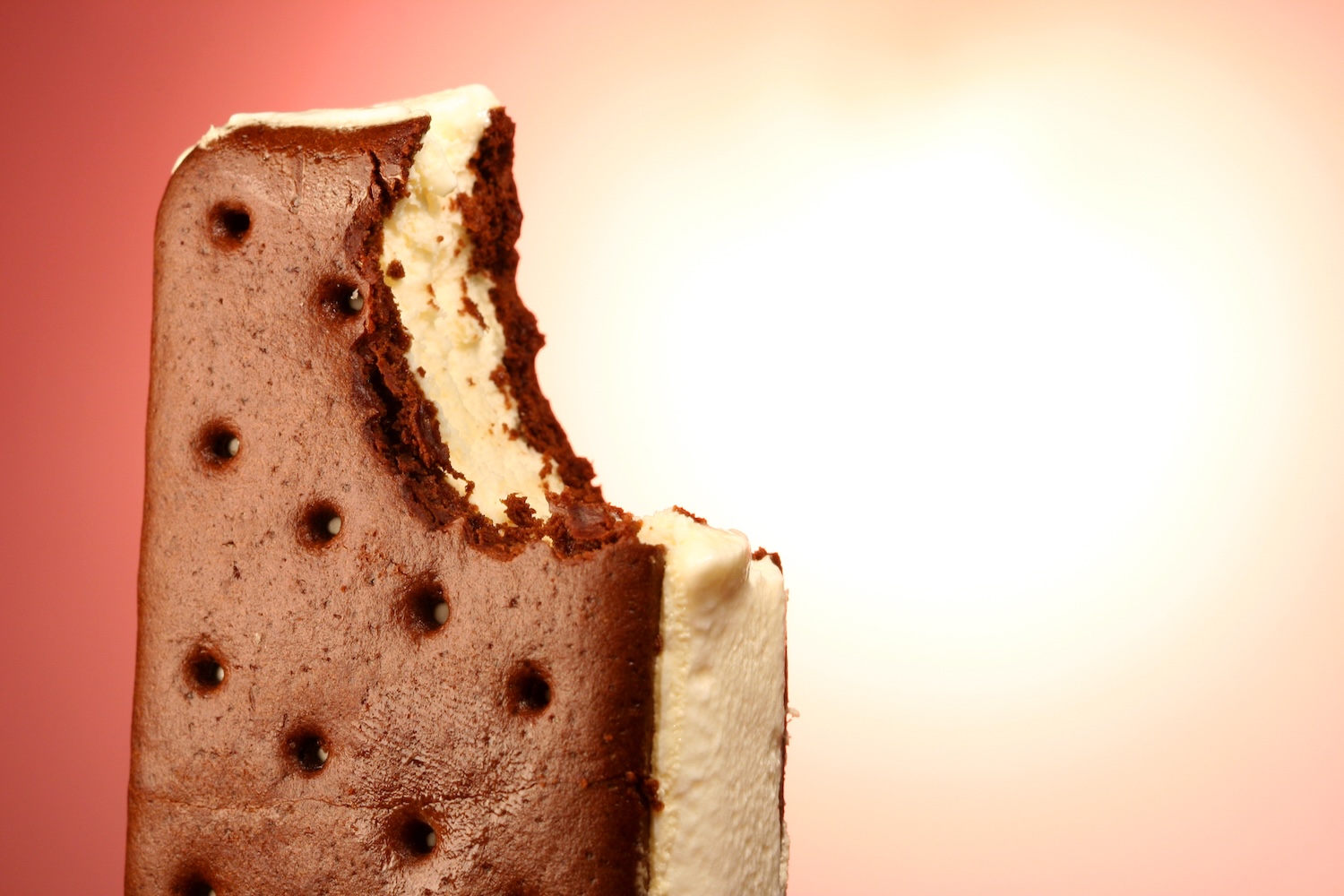 Close-up of a partially eaten ice cream sandwich with chocolate cookies and vanilla ice cream against a gradient background.