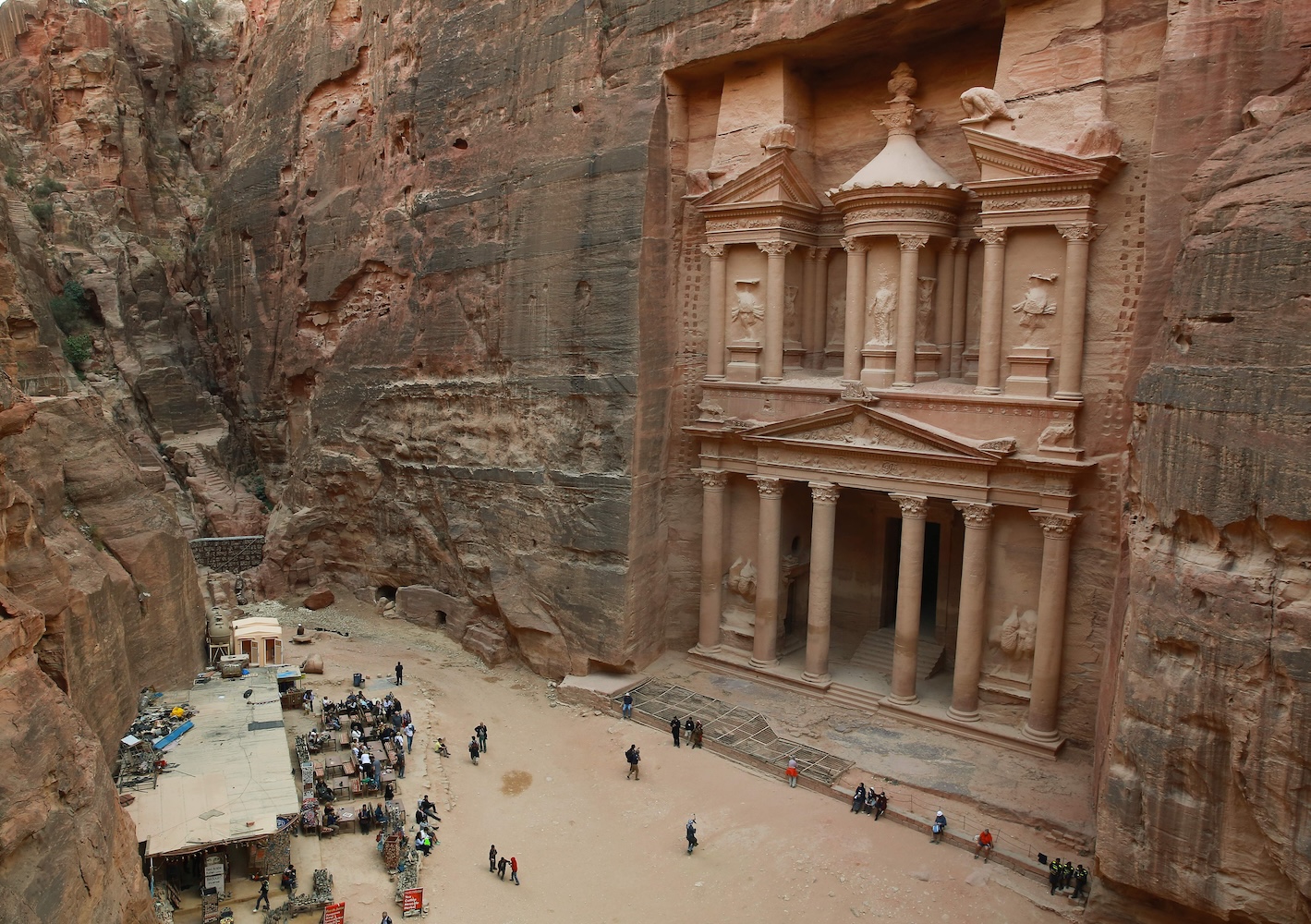 The image shows the Khaznah, or Treasury, in Petra, Jordan, with its ornate rock-cut façade towering over tourists and a small market in the canyon below.