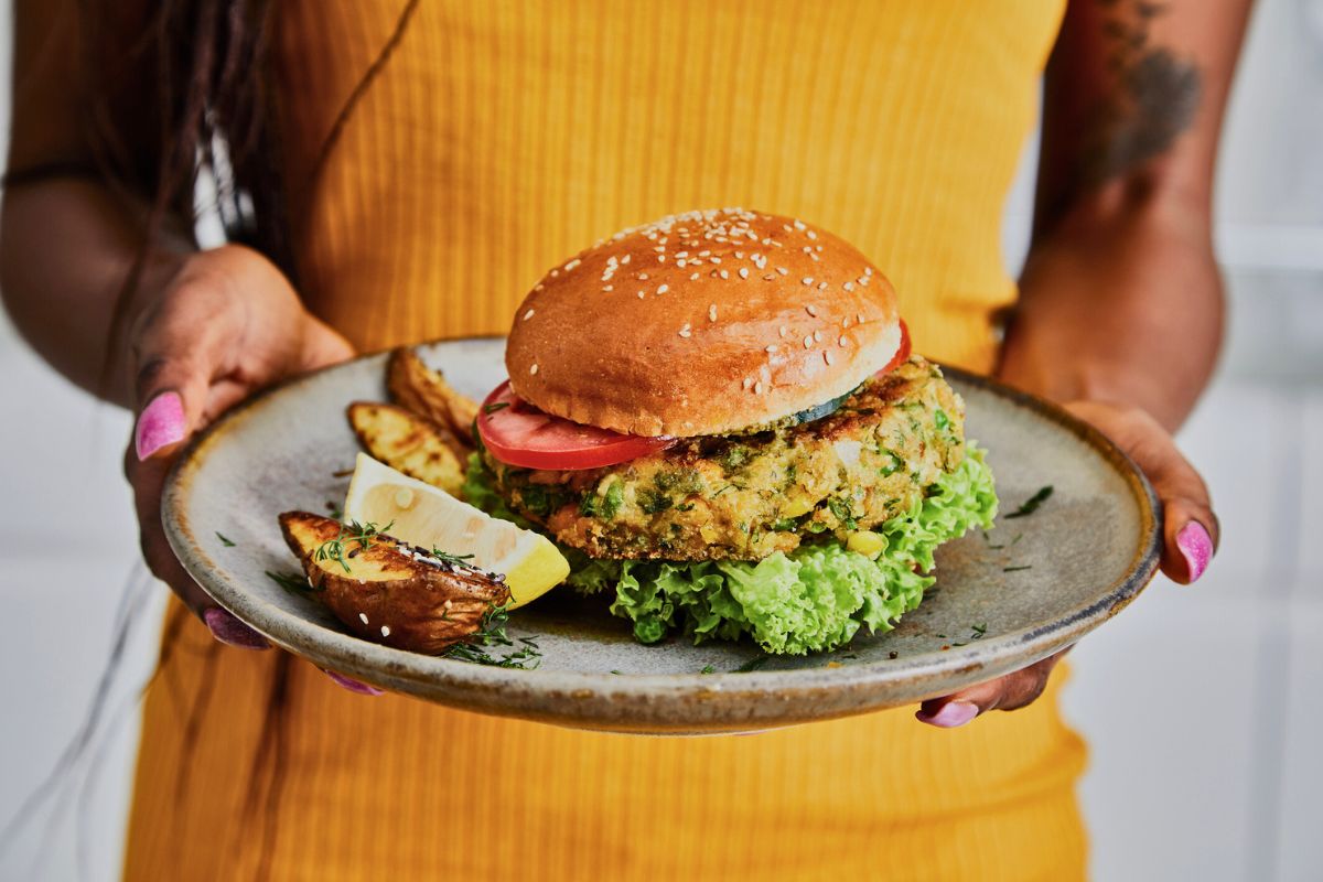 woman holding a plate with vegan burger and wedge fries