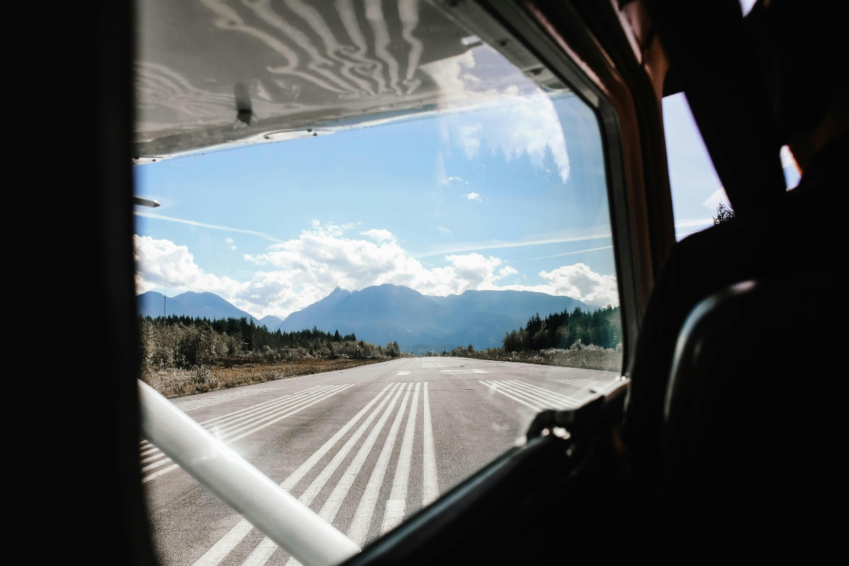 View from inside a small plane on a runway with mountains in the distance under a partly cloudy sky.