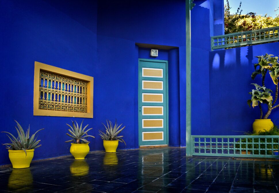 the walls of a unit within the Kardin Marjorelle in Marrakech, Morrocco adorned in their famous blue paint with yellow and teal details of plant pots, window and door trimmings 