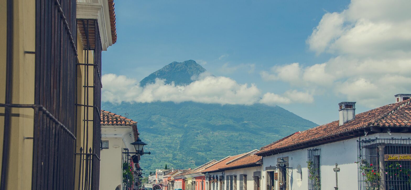 Antigua, Guatemala, one a clear day with a mountain in the clouds in the background.