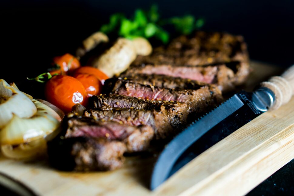 Steak, medium on a plate with tomatoes and herbs.