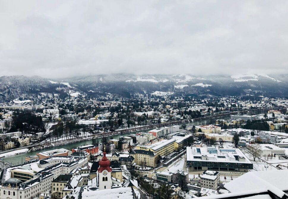 A wide shot of Salzburg, Austria. Rooftops have been dusted lightly with snow, and the sky is cloudy. 