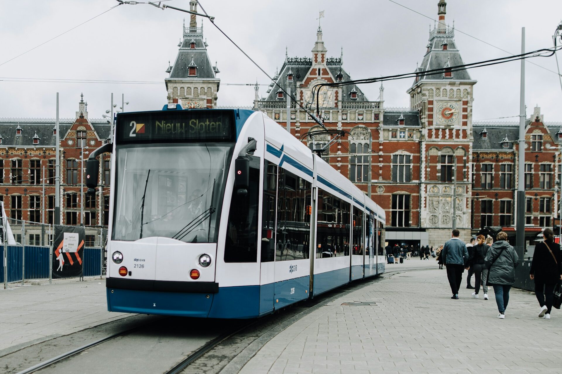 People walking on the sidewalk in Amsterdam near white and blue train during daytime