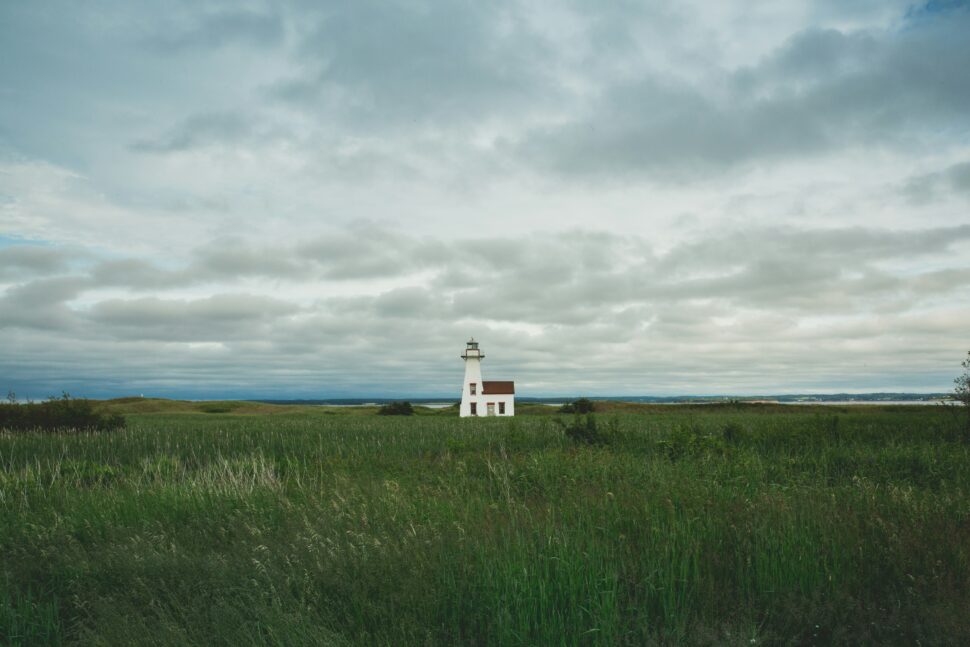 A white lighthouse in a wide, grassy field 