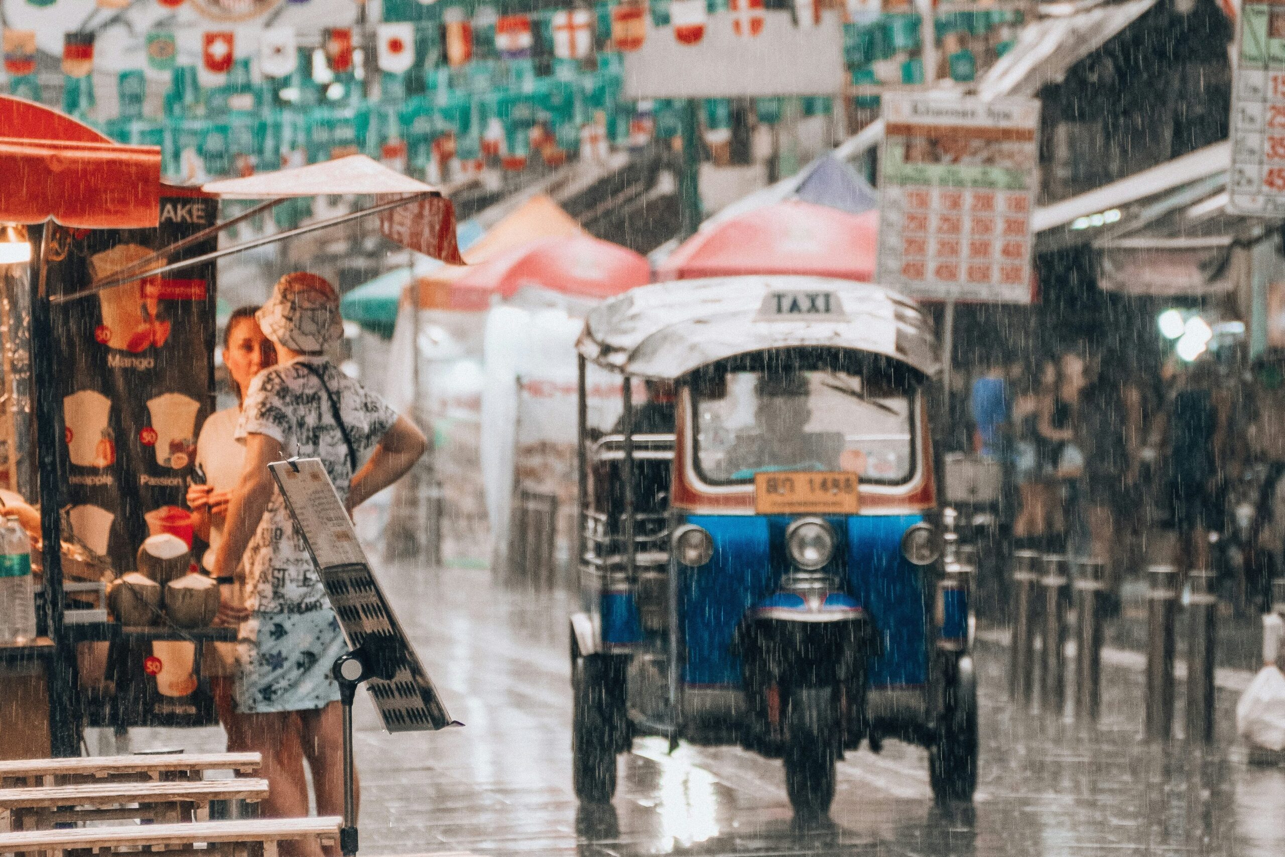 A small taxi drives down Khao San Road in Bangkok in heavy rain. 