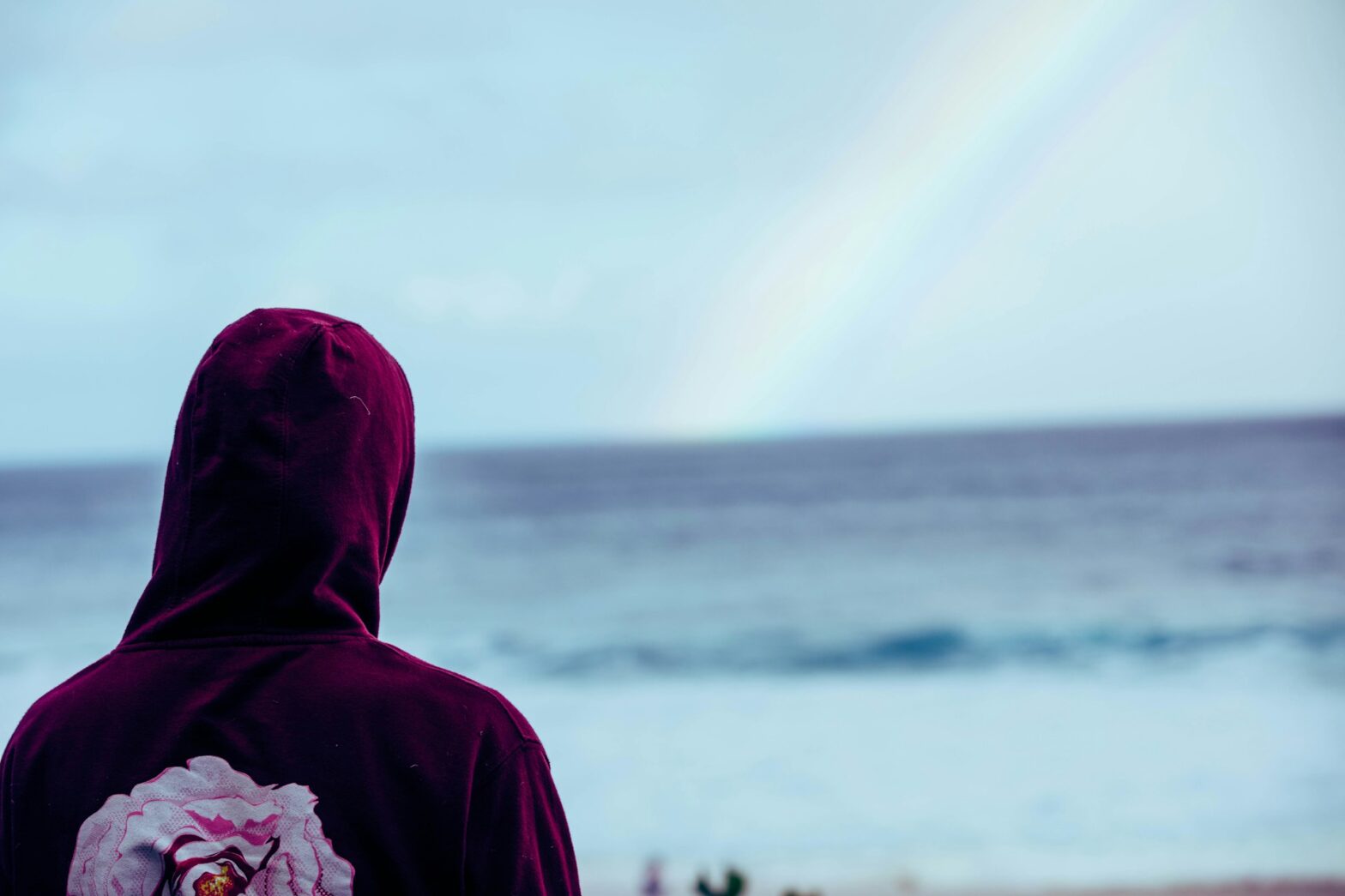 Person in purple hoodie with pink flower on back near water