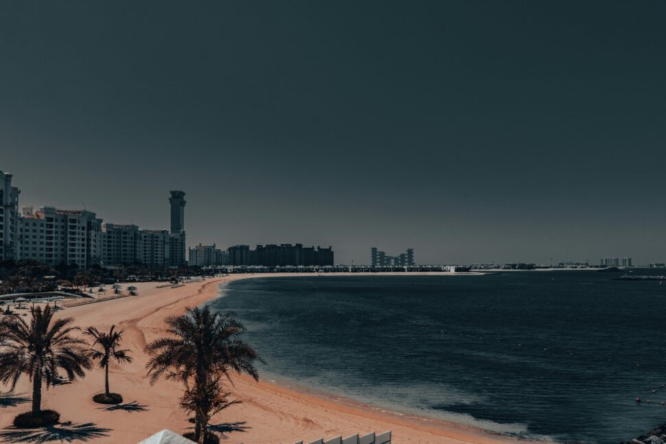 Dubai's cityscape over-looking the coast with sunny skies and palm trees.