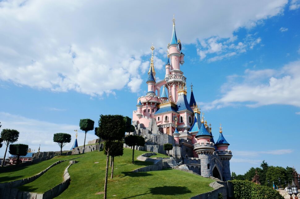 The iconic pink castle at Disneyland Paris, surrounded by trees and a clear blue sky