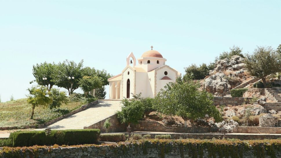 A scenic view of a monastery atop a hill in Crete, with lush landscape and stone pathways for the spring season.