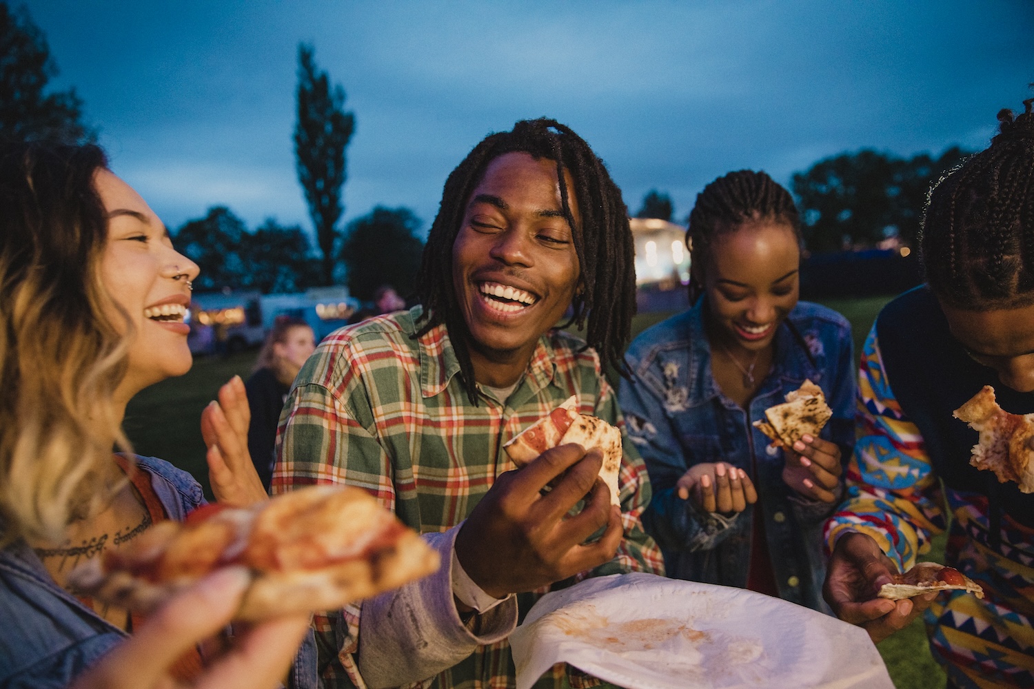 A young group of friends laughing and sharing pizza at a food festival.