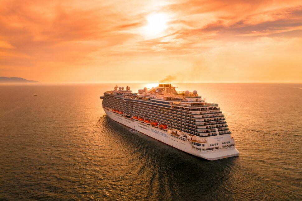 Aerial perspective of a cruise ship with multiple decks pools seen sailing toward the sunset.