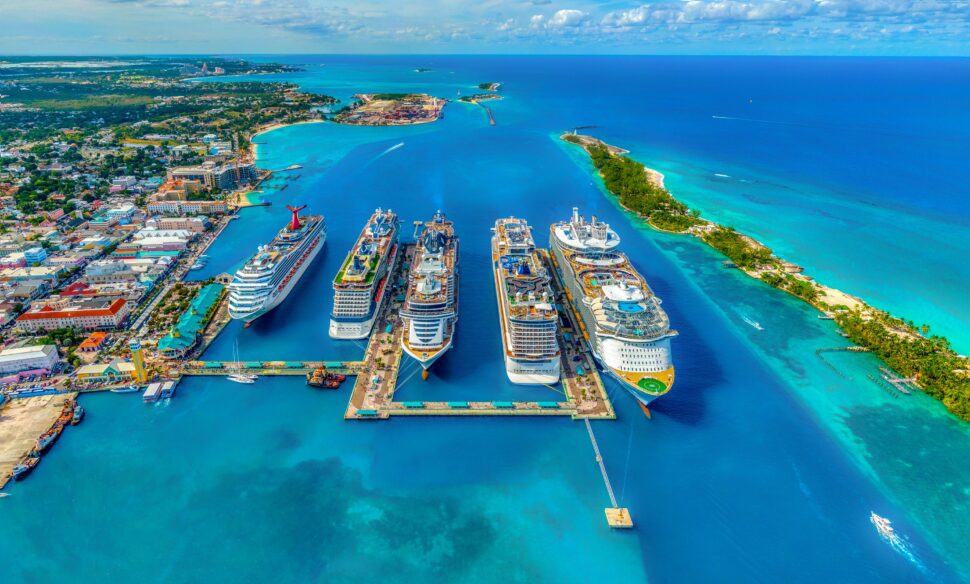 Bird's-eye view of four Norwegian Cruise Line ships docked in the harbor, aligned neatly in a row, with clear blue water surrounding them.