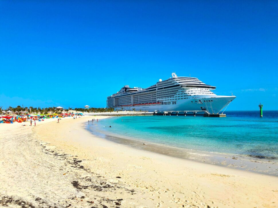 MSC Cruises ship parked on a sunny beach with clear blue skies, surrounded by vast open water.