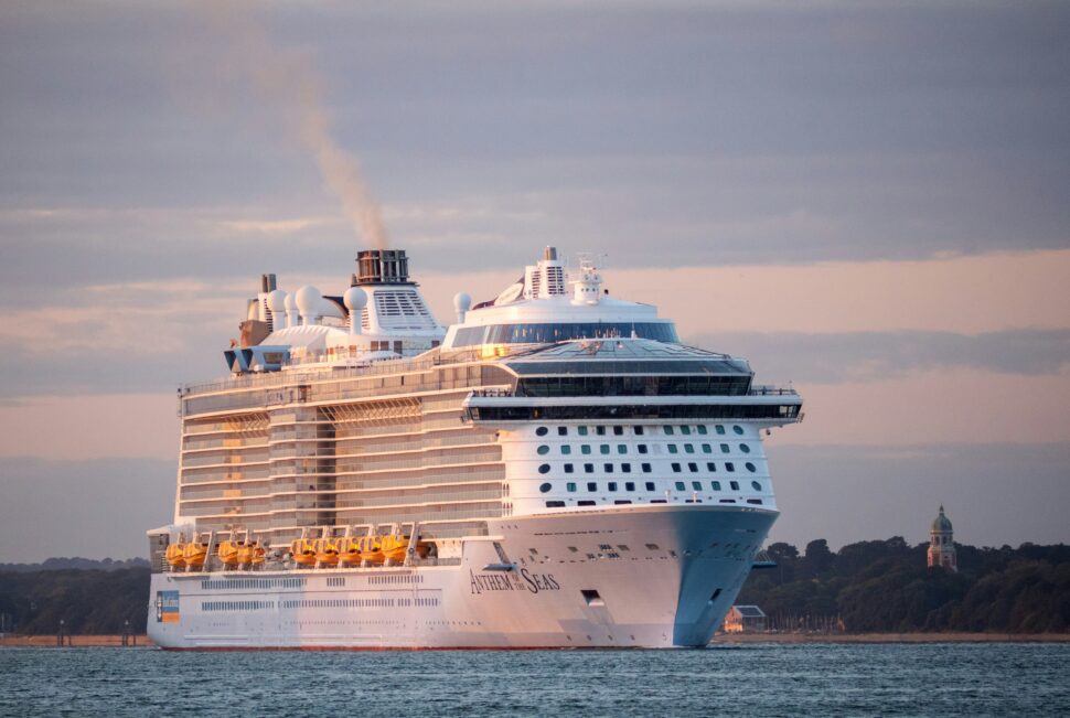 A view of a large cruise ship at sunset, with warm orange and pink in the sky.