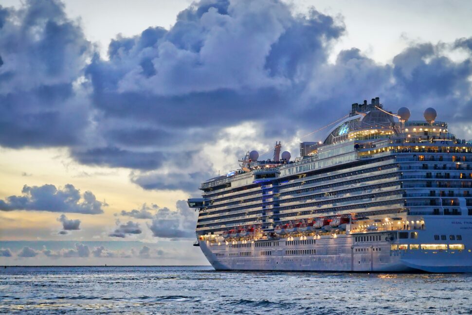 Luxury cruise ship on the water at sunset, with vibrant lights illuminating the ship as the sky transitions to twilight.