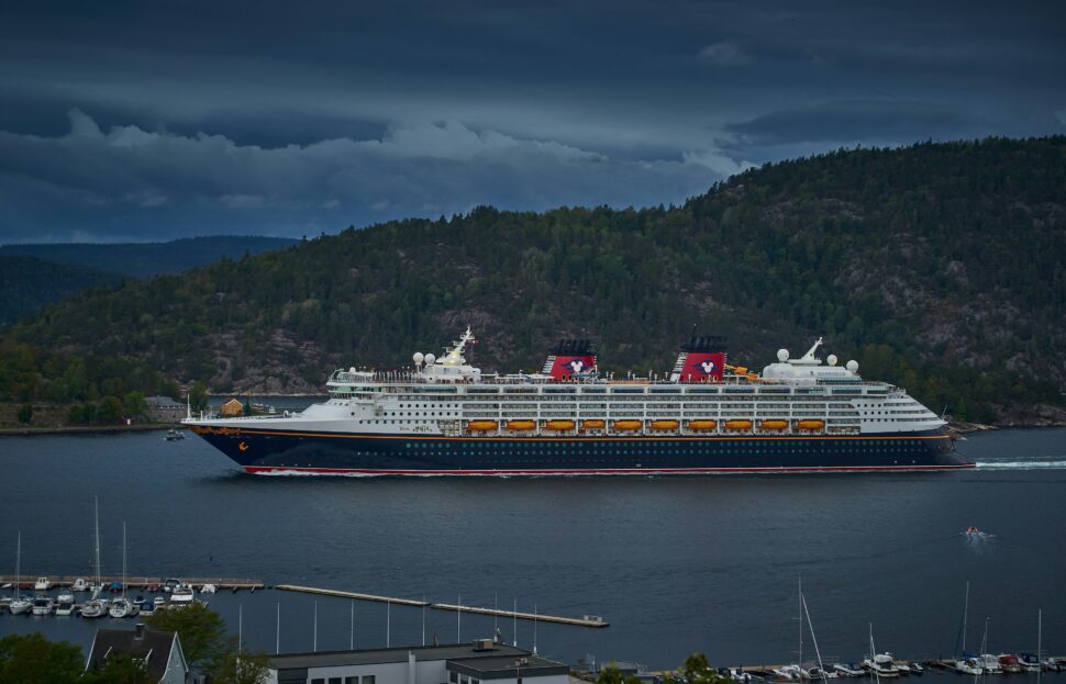 A luxury cruise liner sailing past rugged coastal cliffs with foggy skies overhead.