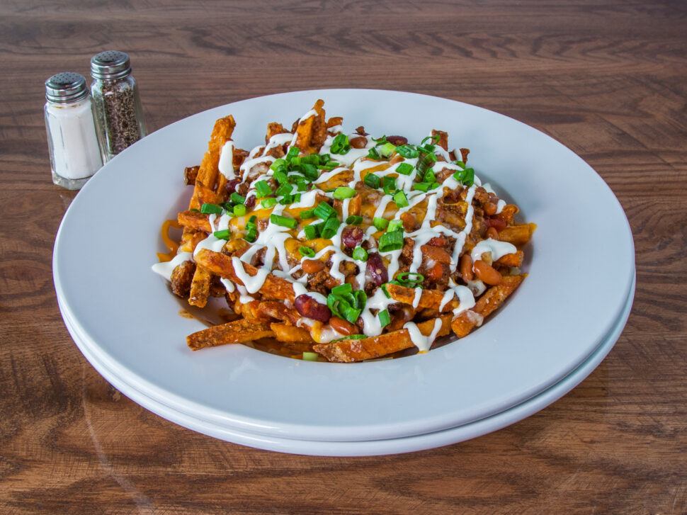 a white round ceramic bowl filled with french fries smothered in chili, bacon cheese and special sauce