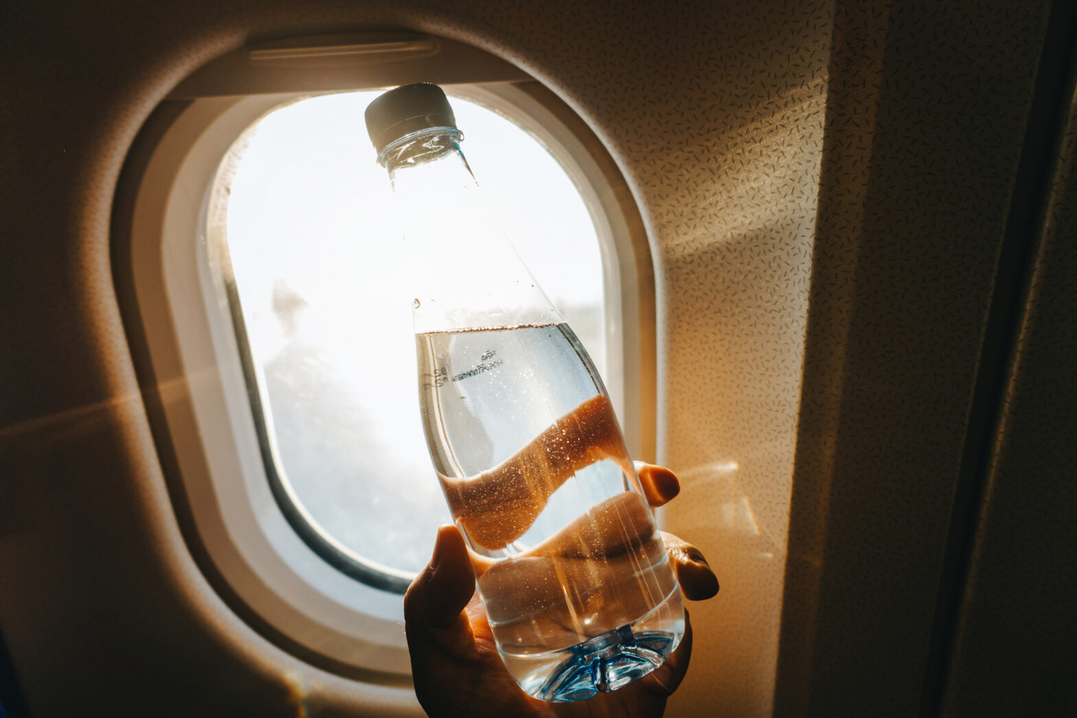 Cropped hand holding a bottle of water against airplane window.