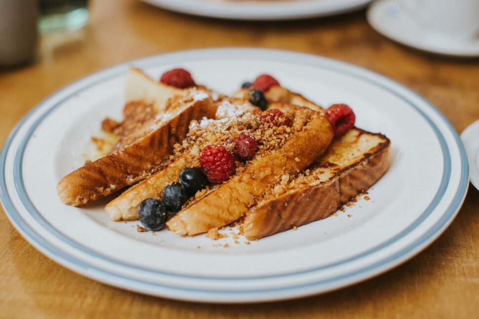 Four slices of French toast with red berries and roasted almonds on top and honey.