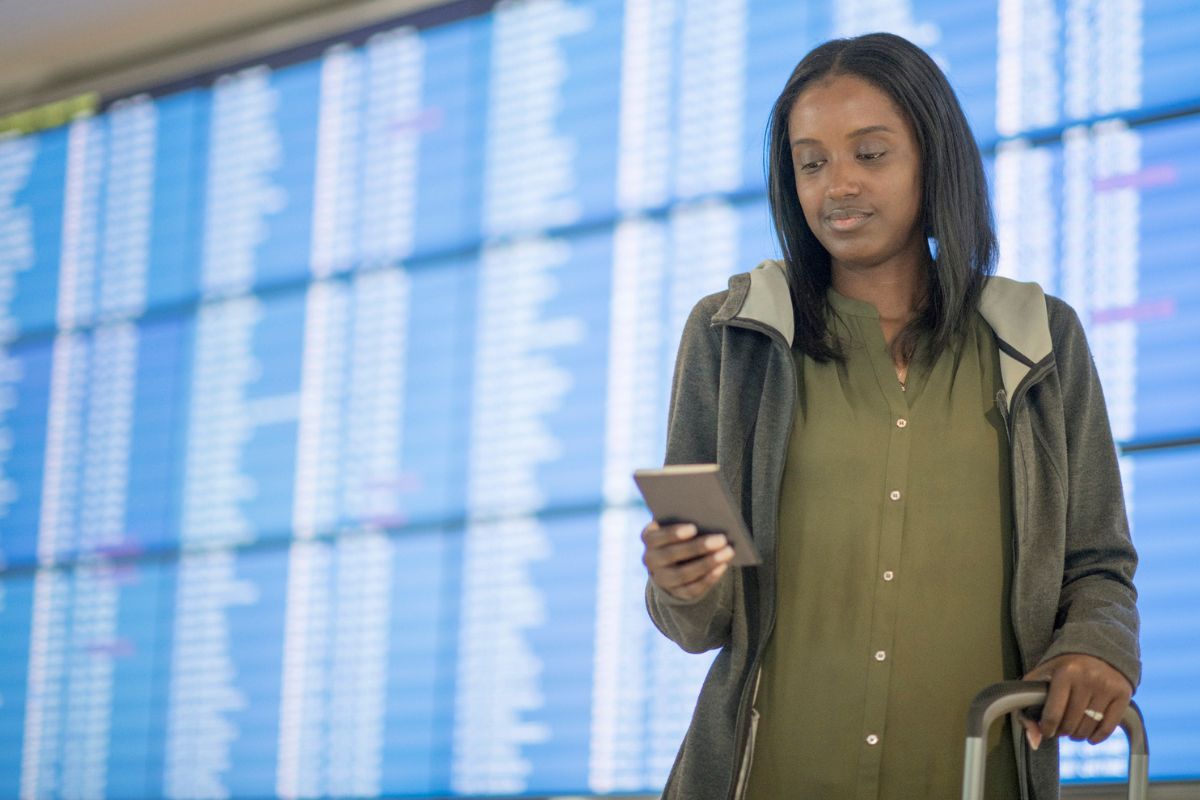 woman looking at phone while standing at the airport with luggage