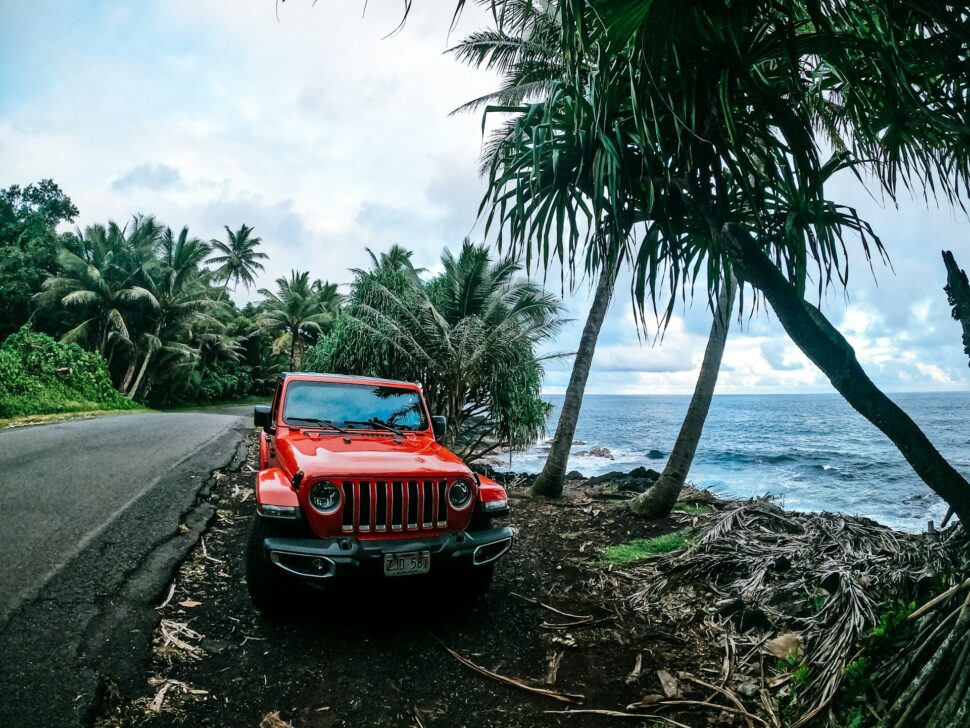 Red SUV truck parked in a dirt path near the beach and palm trees