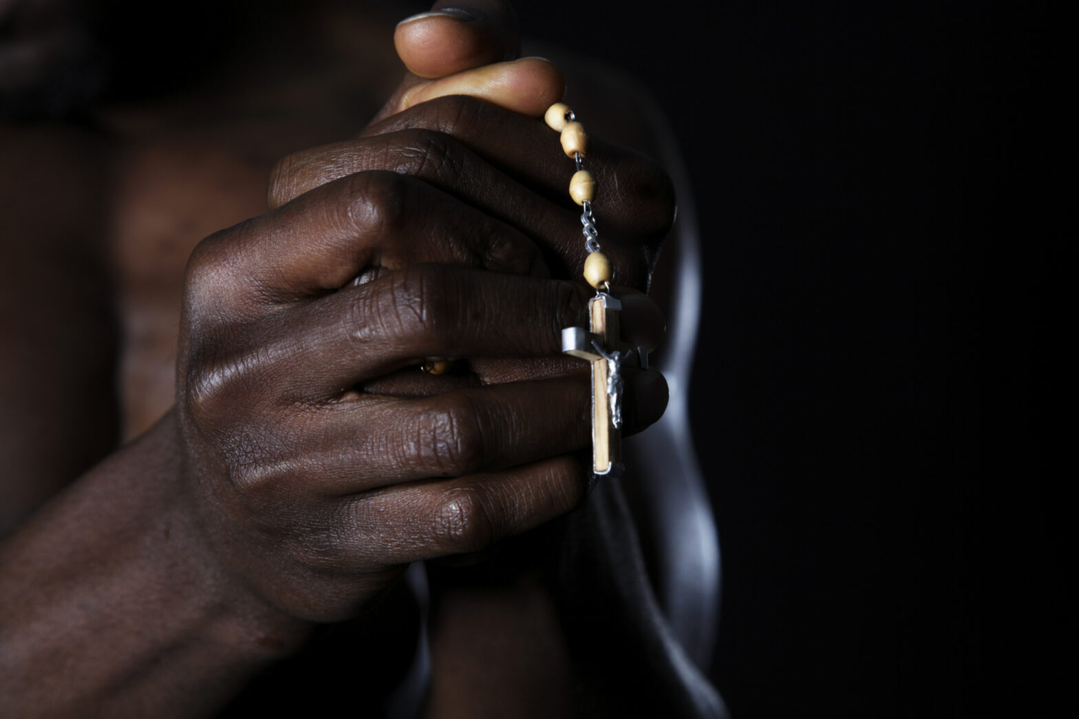 Male hands holding rosary and crucifix. Low key lighting