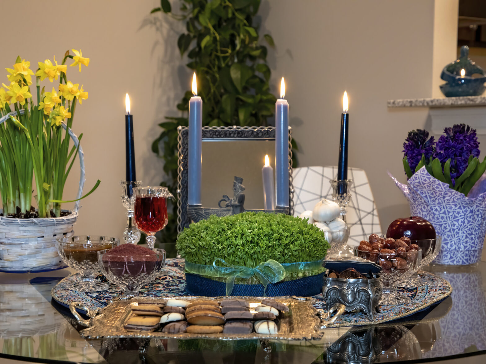 A Haft-Sin table for Nowruz with symbolic items, lit candles, a mirror, and fresh flowers.