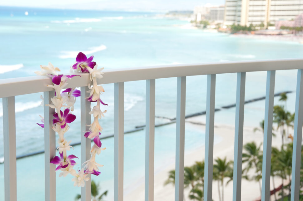 Hawaiian Lei hanging on a hotel balcony with the Pacific Ocean and Waikiki beach in the background.