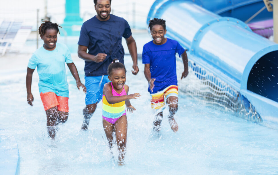 An African-American father and his three children having fun playing at a water park.