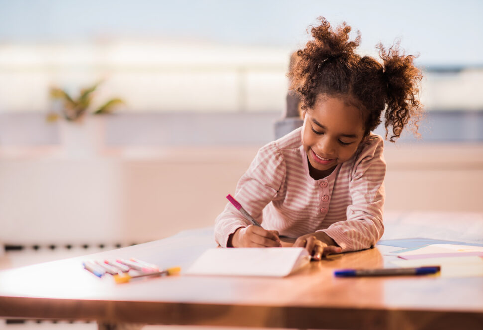 Young girl relaxing on the table at home and coloring in notebook.