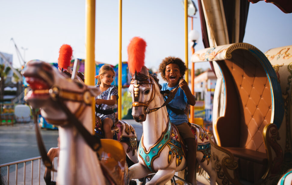 Boy and girl having fun riding horses on amusement park carousel ride.