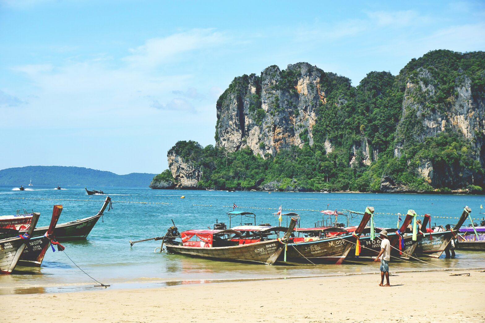 limestone cliffs behind four boats on the shores of Krabi, Thailand
